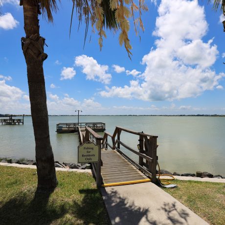 A tranquil scene of the resort's fishing pier as the sun sets over the water, casting a golden glow on the bay at Copano Bay RV Resort in Rockport, TX.