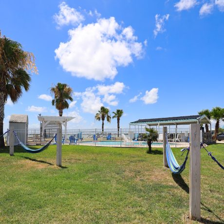 Hammocks and palm trees in a grassy area at Copano Bay RV Resort, Rockport, TX, creating a serene outdoor retreat.