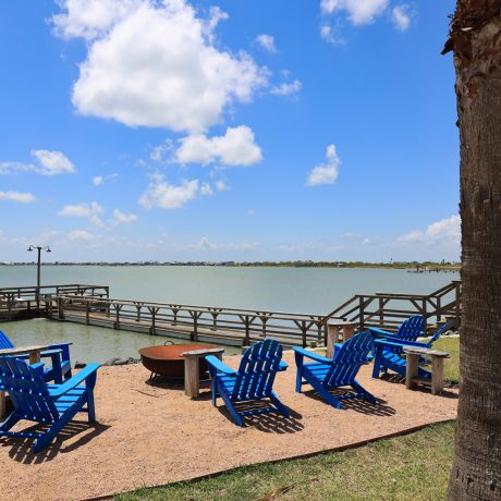 A serene dock at Copano Bay RV Resort, featuring chairs and a fire pit, overlooking a tranquil lake in Rockport, TX.