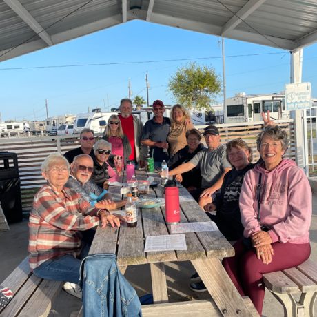 A group of people enjoying a meal together at a picnic table at Copano Bay RV Resort in Rockport, TX.