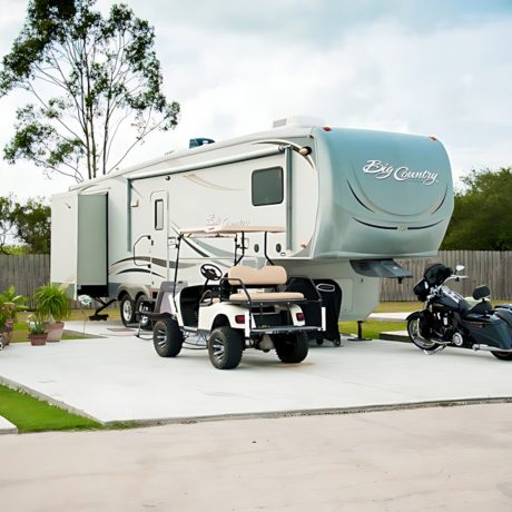 A RV and motorcycle parked side by side at Copano Bay RV Resort in Rockport, TX, under a clear blue sky.